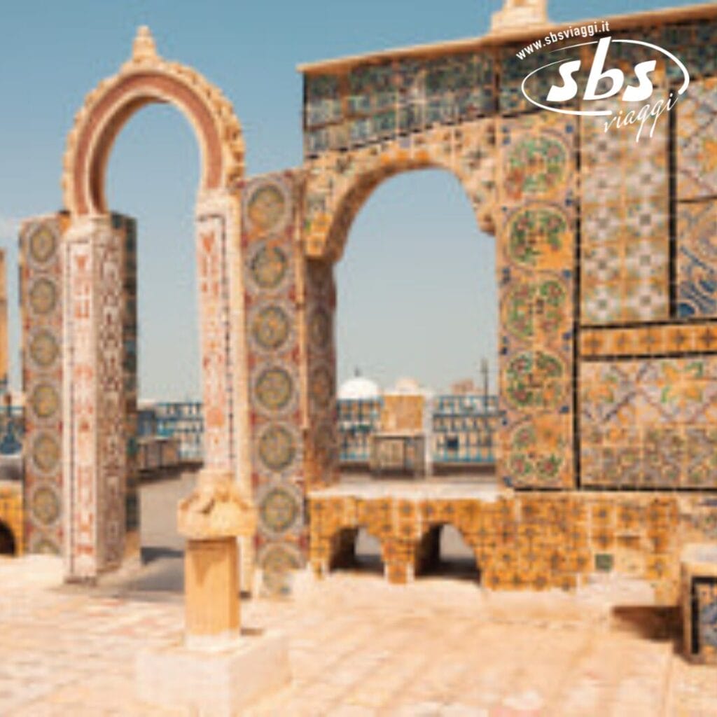 Una struttura con archi e muri in pietra decorati si erge con grazia sotto il cielo terso di Hammamet. Il logo