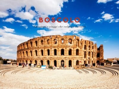 Antico anfiteatro romano sotto un cielo azzurro brillante nel cuore del deserto tunisino, con la scritta "Boscolo" e il testo in italiano sovrapposti.