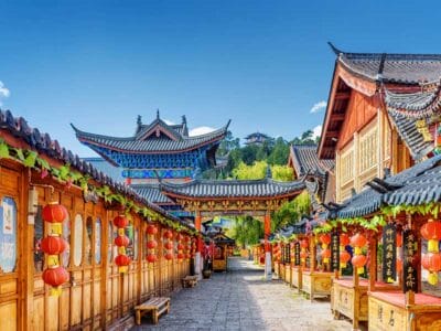 Una colorata strada tradizionale cinese con edifici in legno, lanterne rosse e un cielo azzurro sopra la testa.