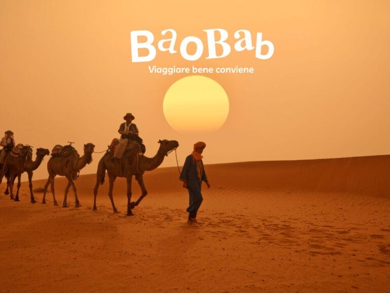Persone con cammelli camminano nel deserto al tramonto, avvolte nella magia del Sahara. Il testo recita: "Baobab, viaggiare bene conviene".