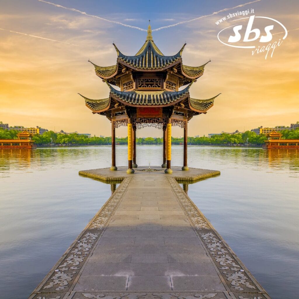 Una pagoda tradizionale si erge alla fine di una passerella su un lago calmo, con un caldo cielo al tramonto che proietta un bagliore sublime sullo sfondo.