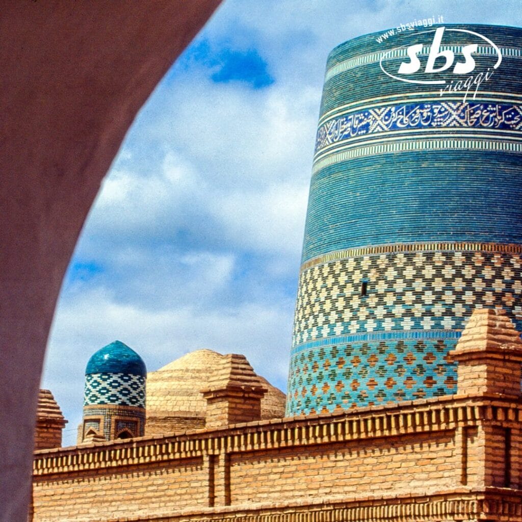 A Khiva, in Uzbekistan, gli edifici in mattoni presentano motivi intricati e cupole blu sotto un cielo nuvoloso, offrendo uno scorcio pittoresco che ricorda una bozza automatica nel design architettonico.