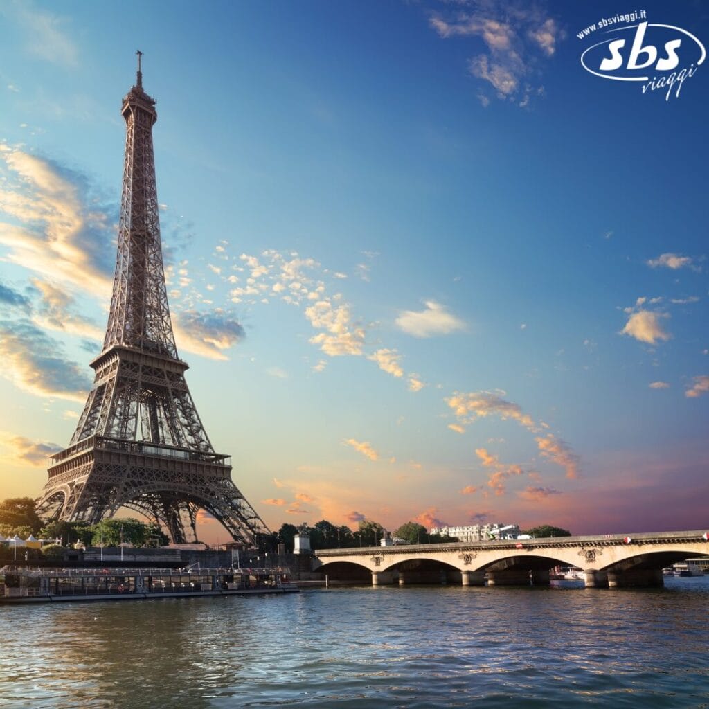 La Torre Eiffel si erge maestosa accanto a un ponte sul fiume al tramonto, con un cielo parzialmente nuvoloso: uno spettacolo tanto affascinante quanto Versailles stessa.
