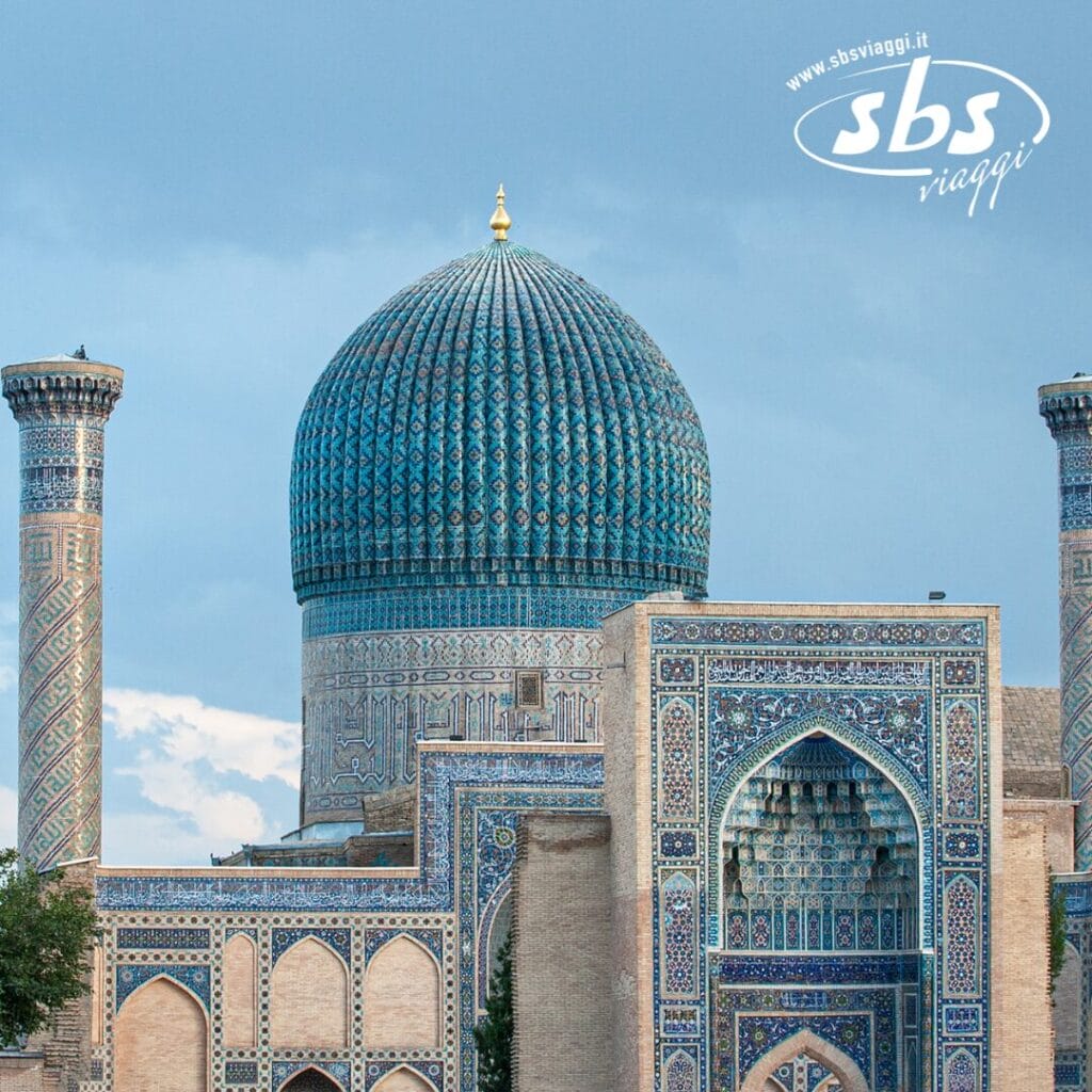 Cupola blu ornata e intricate piastrelle di un edificio storico islamico con minareti, sullo sfondo di un cielo nuvoloso, che ricorda Bozza automatica. Logo nell'angolo.