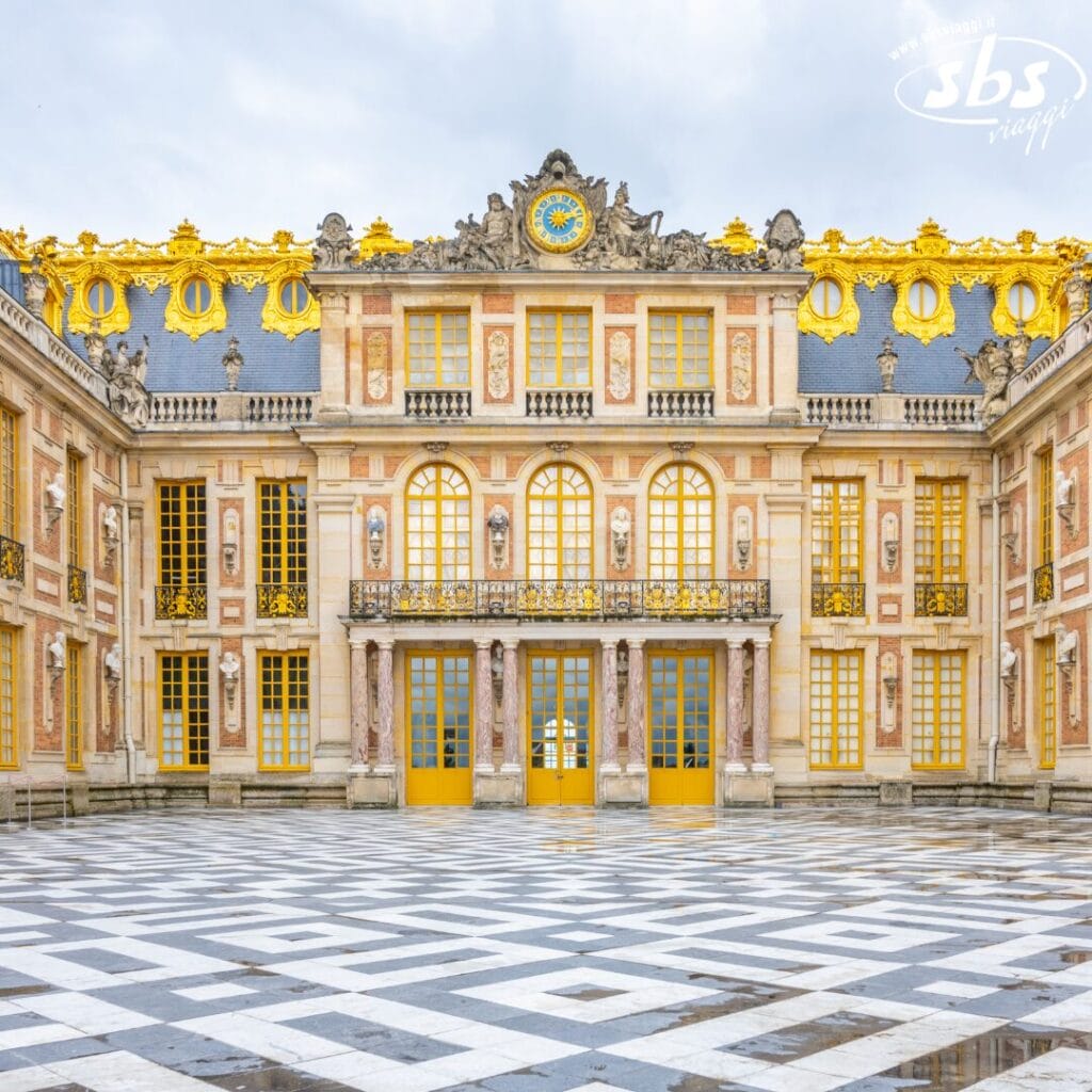 Vista esterna del Palazzo di Versailles a Parigi, che mostra una facciata simmetrica impreziosita da dettagli dorati e un cortile decorato.