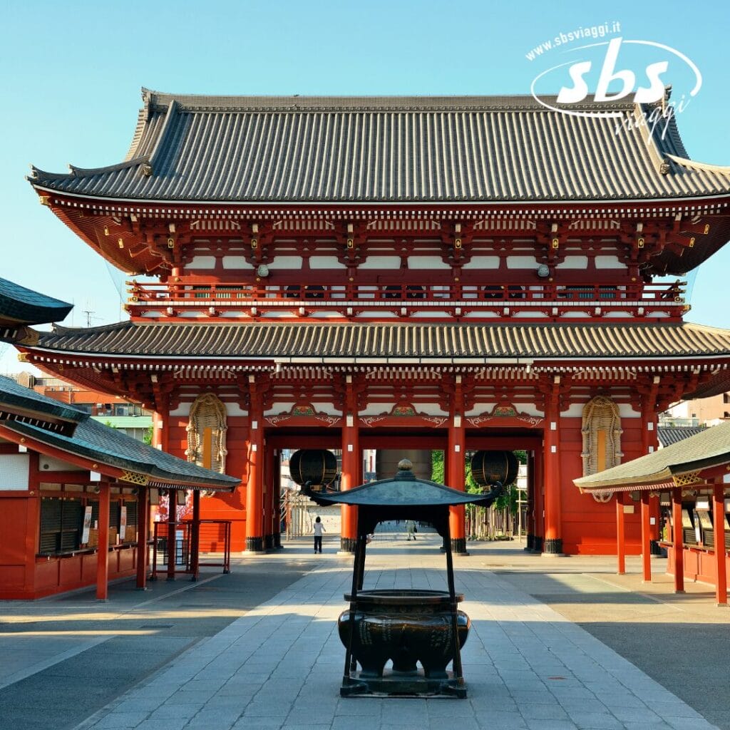 Il tempio tradizionale giapponese rosso, completo di tetto decorato, si erge fiero sotto un cielo azzurro e limpido. Una bozza automatica sussurra storie antiche mentre un sentiero in pietra guida i visitatori al grande incensiere all'ingresso.