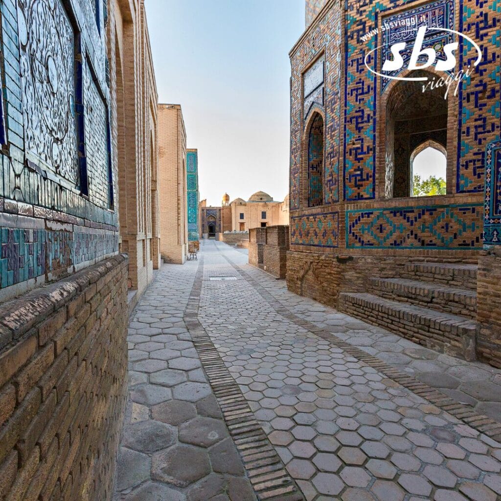 Uno stretto sentiero in pietra fiancheggiato da edifici in mattoni blu e marroni finemente piastrellati sotto un cielo limpido, come uno schizzo di bozza automatica portato in vita. Una serie di archi e piastrelle decorative sulla destra conduce a un cortile aperto.