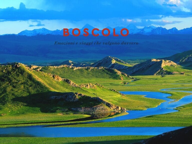 Un fiume sinuoso scorre attraverso verdi colline con montagne innevate sullo sfondo e un cielo azzurro: uno scenario ideale per la tua prossima avventura nel Tour Cina.