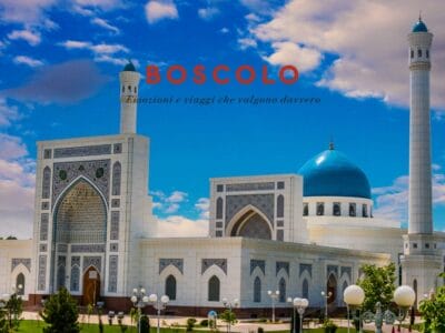 Una moschea bianca con cupole blu sotto un cielo luminoso, che evoca la grandiosità dell'Uzbekistan, con la scritta "Boscolo" e il testo in italiano sopra.