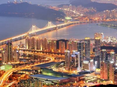 Il paesaggio urbano di Busan di notte abbaglia con grattacieli illuminati, ponti e corsi d'acqua. Le luci urbane vibranti creano un layout dinamico contro le colline e il mare, simile a una bozza automatica, una bozza perfetta di natura e architettura in armonia.
