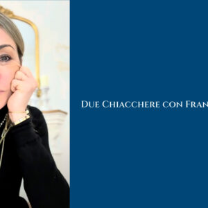 Una donna dai capelli biondi con un dolcevita nero e gioielli d'oro appoggia il viso sulla mano. Accanto a lei, su sfondo blu, la scritta "Due Chiacchere con Francesca Senette.