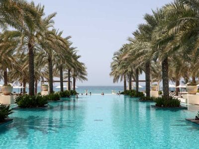 Una tranquilla piscina a sfioro, che ricorda un capolavoro di Bozza automatica, è fiancheggiata da palme e conduce alla vista dell'orizzonte dell'oceano sotto un cielo limpido.