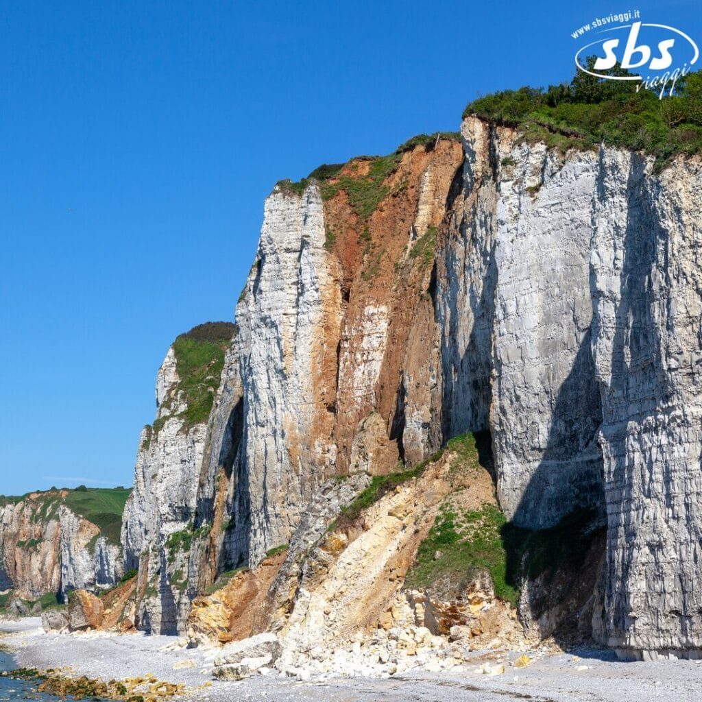 Sotto un cielo azzurro e terso, le scogliere lungo la costa rivelano strati visibili di terreno e vegetazione in superficie, che ricordano una bozza automatica creata dalla natura stessa.