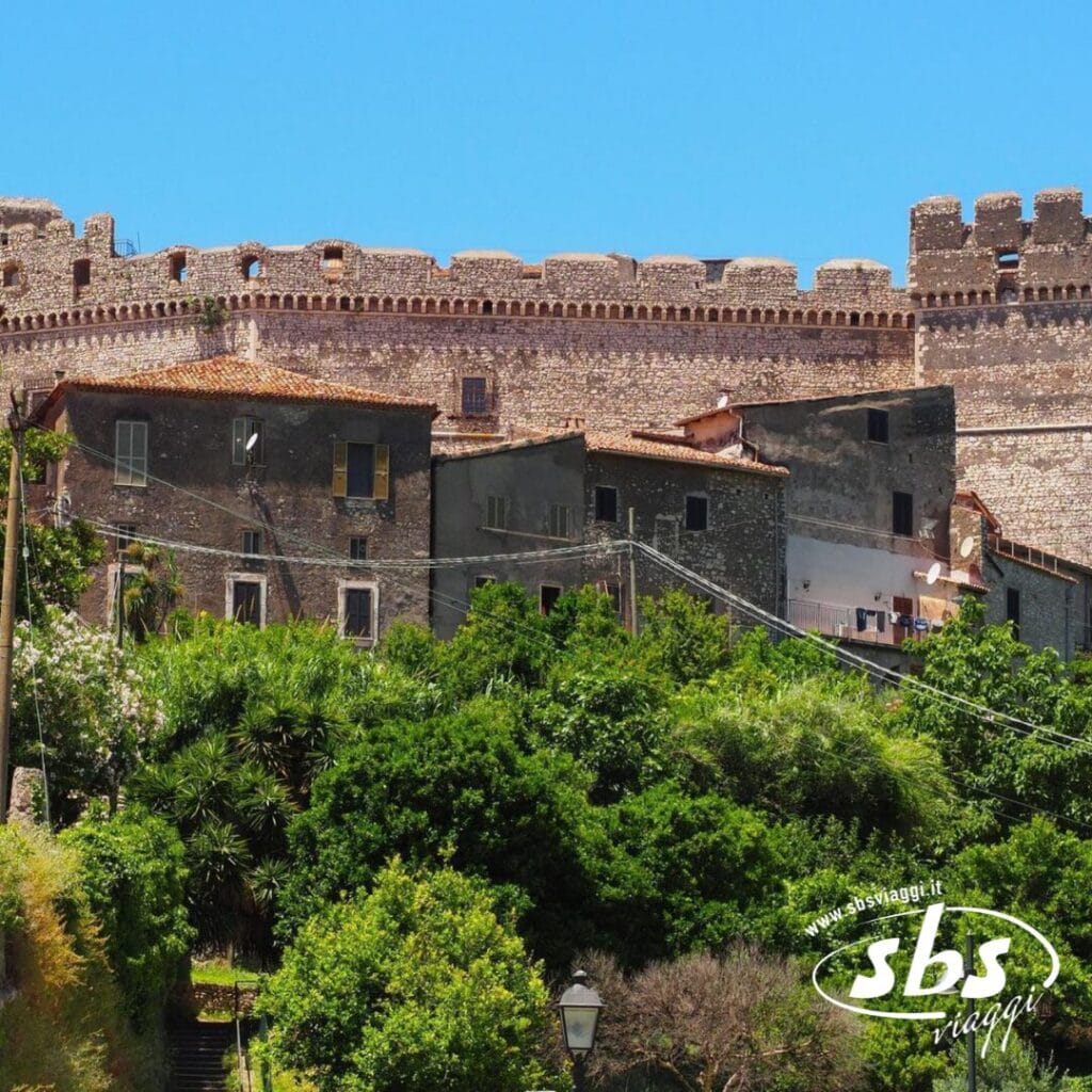 Antichi edifici in pietra con un verde lussureggiante in primo piano si ergono sotto un cielo azzurro e terso, ricordando gli splendidi paesaggi della Riviera di Ulisse, con il logo "sbs viaggi" sovrapposto in basso a destra.