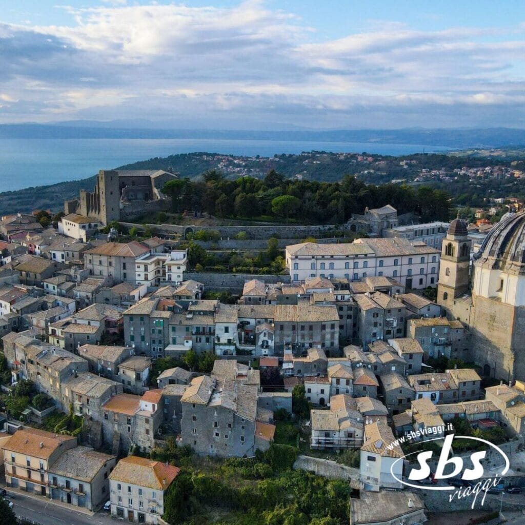 Vista aerea della città storica, che ricorda il fascino etrusco, con edifici in pietra, una chiesa e una fortezza in cima alla collina. Il Tour della Tuscia rivela la sua bellezza contro la lontana costa e il mare esteso sotto un cielo nuvoloso.