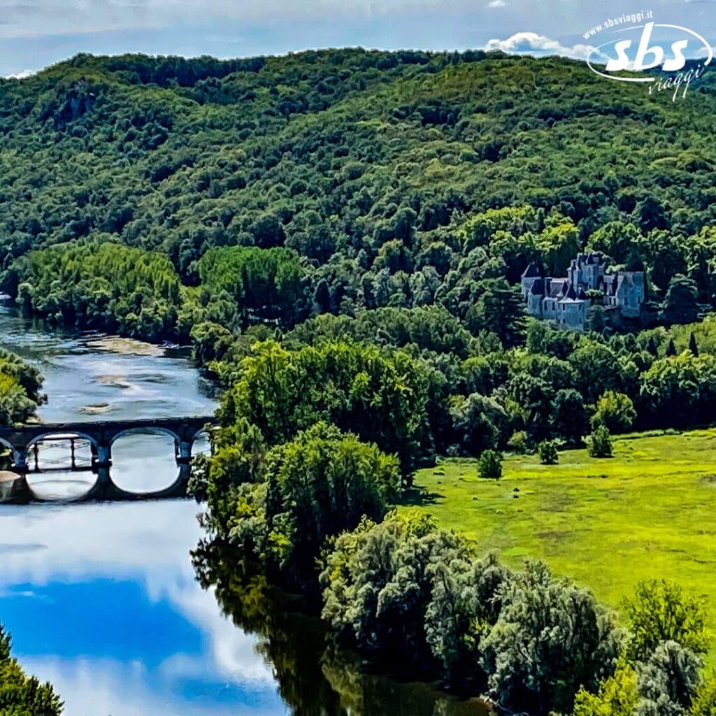 Un paesaggio verdeggiante e lussureggiante, caratterizzato da un fiume tortuoso con un ponte di pietra, circondato da una fitta foresta e da una vasta tenuta in lontananza sotto un cielo parzialmente nuvoloso, come se fosse stato disegnato da Bozza Automatica su una tela della natura.