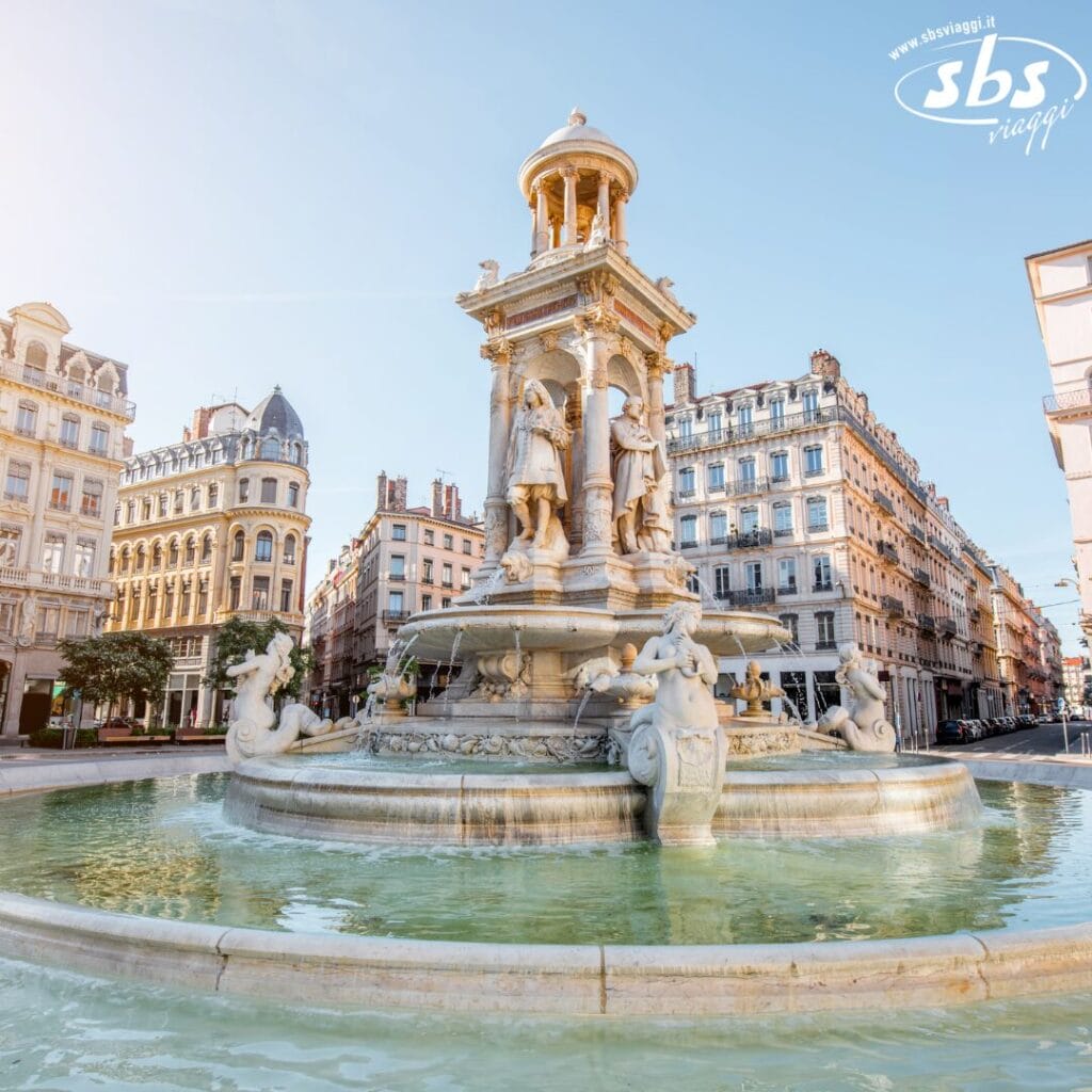 Fontana con statue ornate e acqua corrente abbellisce una piazza cittadina nel cuore di Grande Sud-Ovest, Francia, circondata da edifici storici. Cielo luminoso e limpido in alto.