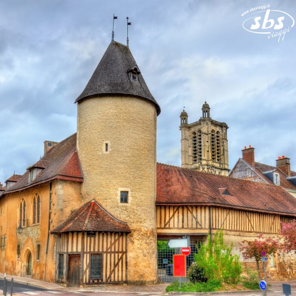 Si dipana uno scenario storico europeo con una torre rotonda e muri a graticcio sotto un cielo nuvoloso, mentre sullo sfondo incombe il campanile di una chiesa in pietra, evocando un'atmosfera che ricorda un capolavoro di Bozza automatica.