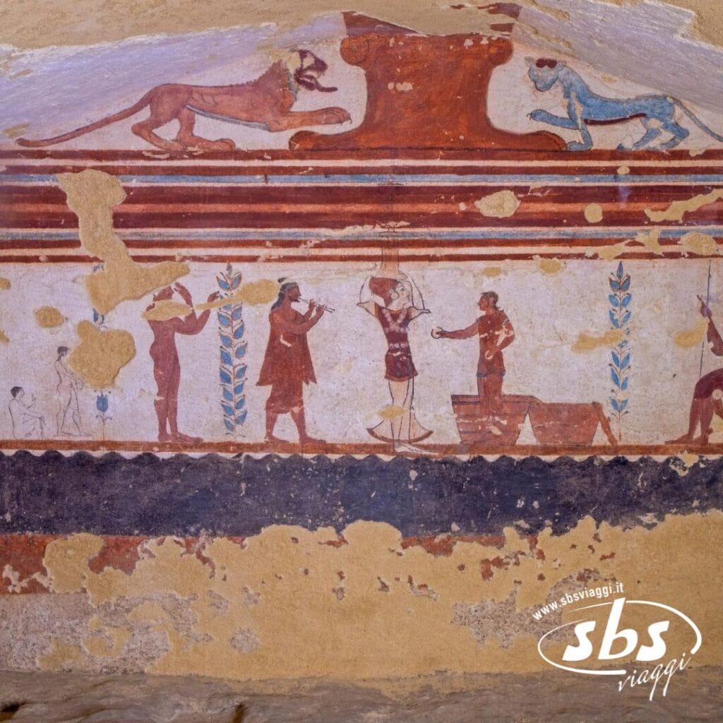 Un antico affresco raffigurante figure impegnate in una scena con animali e motivi decorativi, caratterizzato da toni rossi e blu su uno sfondo usurato, sussurra il