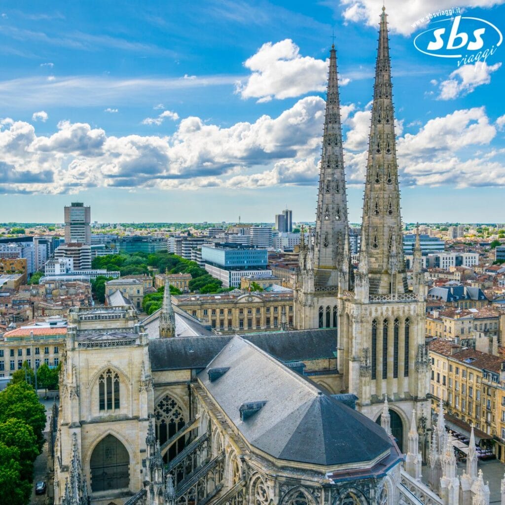 Vista aerea della cattedrale di Bordeaux nel Grande Sud-Ovest della Francia, con le sue maestose torri circondate da edifici cittadini sotto un cielo azzurro parzialmente nuvoloso.