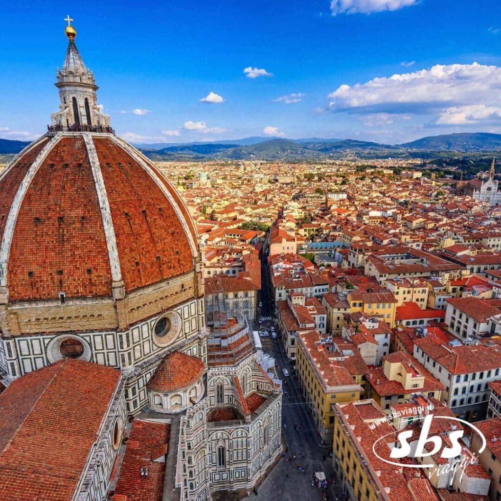 Vista aerea di Firenze, Italia, che mette in mostra la cupola di tegole rosse del Duomo di Firenze e gli edifici circostanti sullo sfondo delle colline lontane sotto un cielo azzurro, offrendo una splendida introduzione al tuo Tour Toscana.