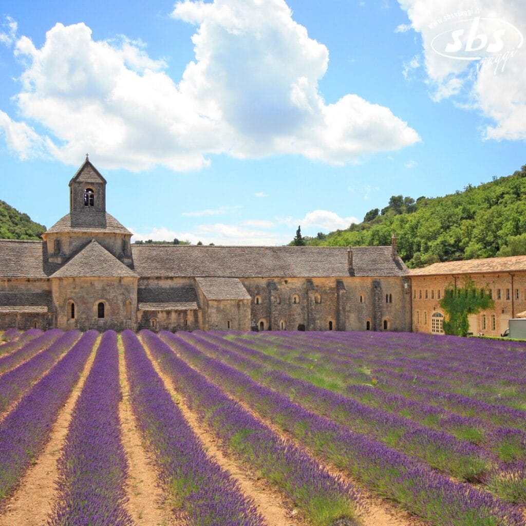 Un campo di lavanda si estende verso una storica abbazia in pietra in una giornata di sole con qualche nuvola, creando la cornice perfetta per una Bozza automatica.