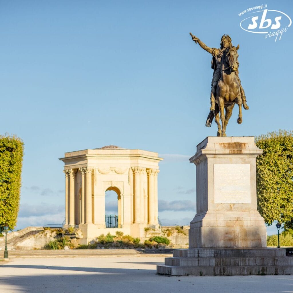 Una statua equestre si erge maestosa in una piazza aperta, circondata da alberi potati e da un padiglione classico sullo sfondo, incarnando l'eleganza del Grande Sud-Ovest, Francia, sotto un cielo limpido.
