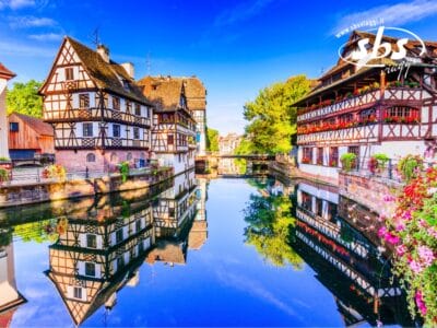 Le case a graticcio si specchiano maestose in un canale tranquillo, circondate da una vegetazione lussureggiante e da un cielo azzurro limpido, creando uno scenario pittoresco che cattura i sensi.