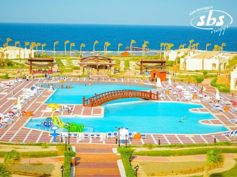 L'area della piscina del resort, dotata di un ponte di legno e circondata da sedie a sdraio, palme ed erba, si affaccia sull'oceano: un perfetto esempio di serena bellezza costiera.