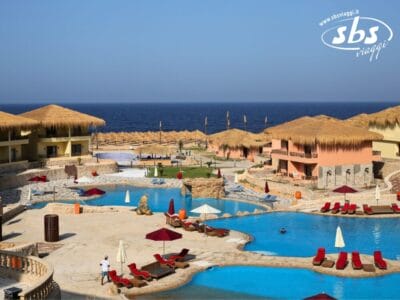 Questo resort tropicale, che vanta numerose piscine e edifici con tetti di paglia adornati da ombrelloni rossi, promette una fuga serena. Passeggiate lungo sentieri in pietra con l'oceano in vista e un cielo azzurro e terso sopra, creando uno sfondo idilliaco che ricorda una "Bozza automatica".