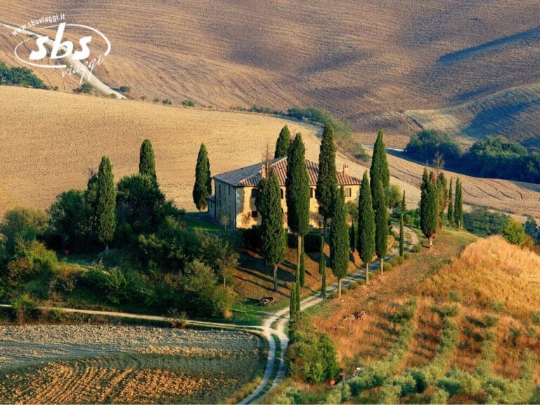 Vista aerea di una casa rustica, immersa tra cipressi e campi, nel pittoresco paesaggio rurale che ricorda il Tour Toscana.