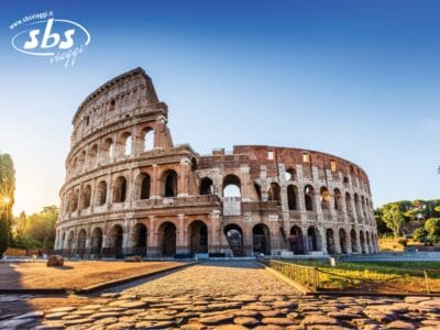 Il Colosseo di Roma si erge maestoso sotto un cielo azzurro e terso, con la luce del sole del mattino che illumina la sua antica struttura in pietra, vero simbolo della Caput Mundi.