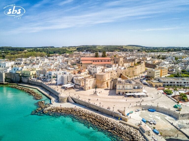 Vista aerea di una cittadina costiera del Salento, con edifici storici in pietra, un lungomare e un mare turchese, circondata da case bianche e verde: uno dei veri tesori del Salento.