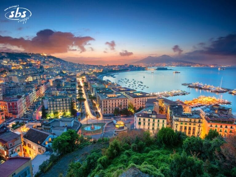 Una città costiera al tramonto, con edifici, strade e luci accanto a una baia tranquilla; sullo sfondo si vedono le montagne sotto un cielo colorato, evocando il fascino senza tempo e i tesori nascosti dei Borboni.