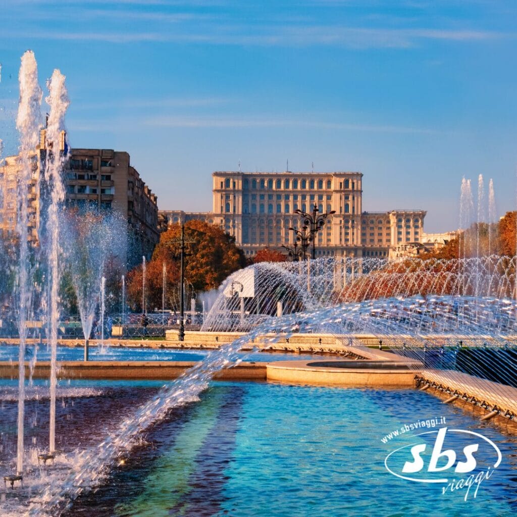 Fontane e piscine in un parco cittadino con un grande edificio storico sullo sfondo; cielo limpido e alberi autunnali visibili: perfetto per chi desidera visitare la Bulgaria o la Romania.