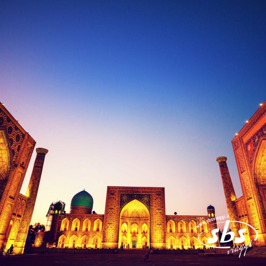 Una vista grandangolare della piazza Registan illuminata di Samarcanda, in Uzbekistan, sulla storica Via della Seta, con la sua intricata architettura islamica e un limpido cielo serale.