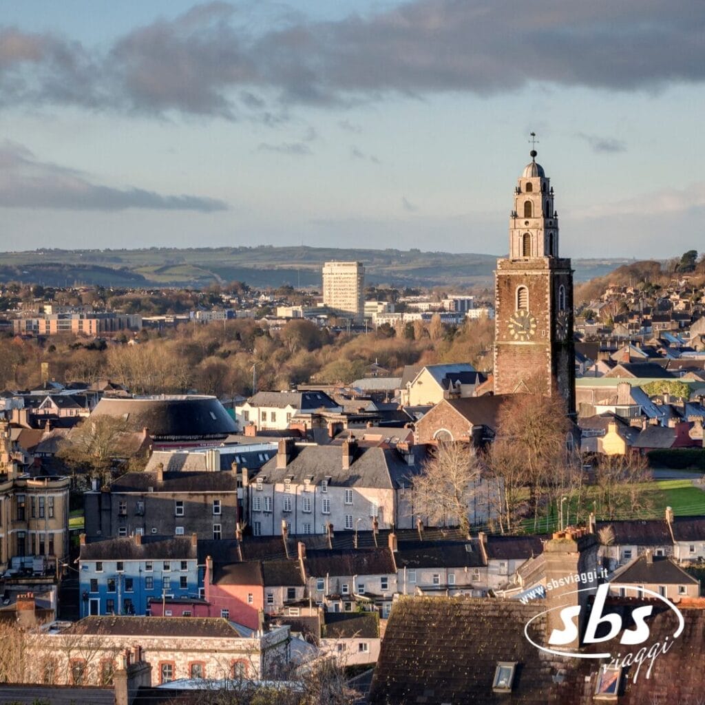 Paesaggio urbano con il campanile della chiesa di Sant'Anna con l'orologio, circondato da edifici e colline sotto un cielo parzialmente nuvoloso, che cattura le bellezze d'Irlanda e ispira viaggi in questa splendida terra.
