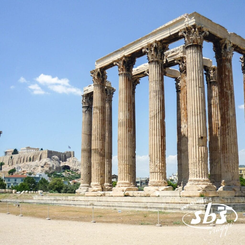 Antiche colonne in pietra del Tempio di Zeus Olimpio ad Atene, in Grecia, con l'Acropoli visibile sullo sfondo sotto un cielo parzialmente nuvoloso: uno dei momenti salienti di ogni Tour Grecia Classica.