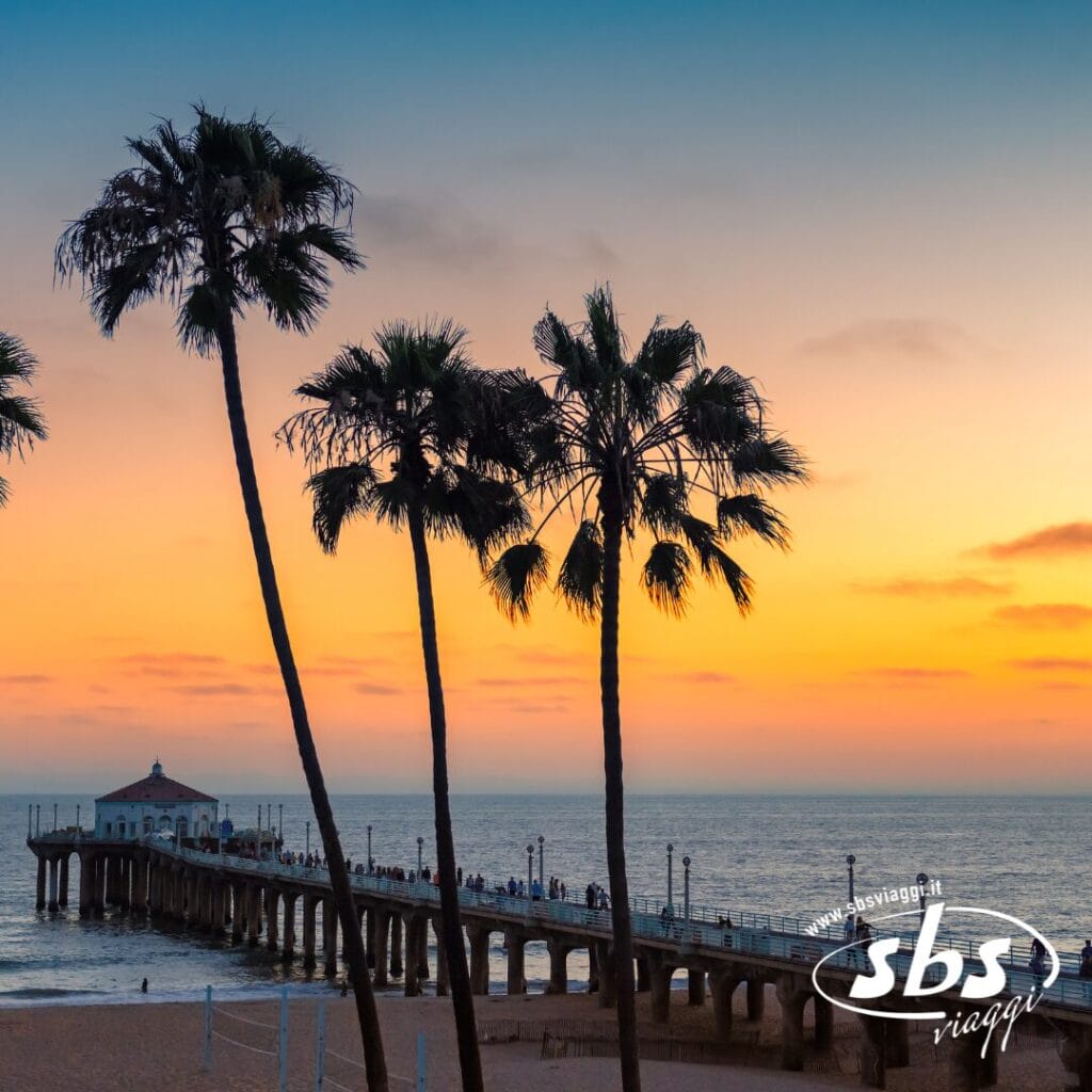 Le palme incorniciano un lungo molo sull'oceano al tramonto a Los Angeles, con persone che passeggiano lungo il molo e una spiaggia in primo piano.