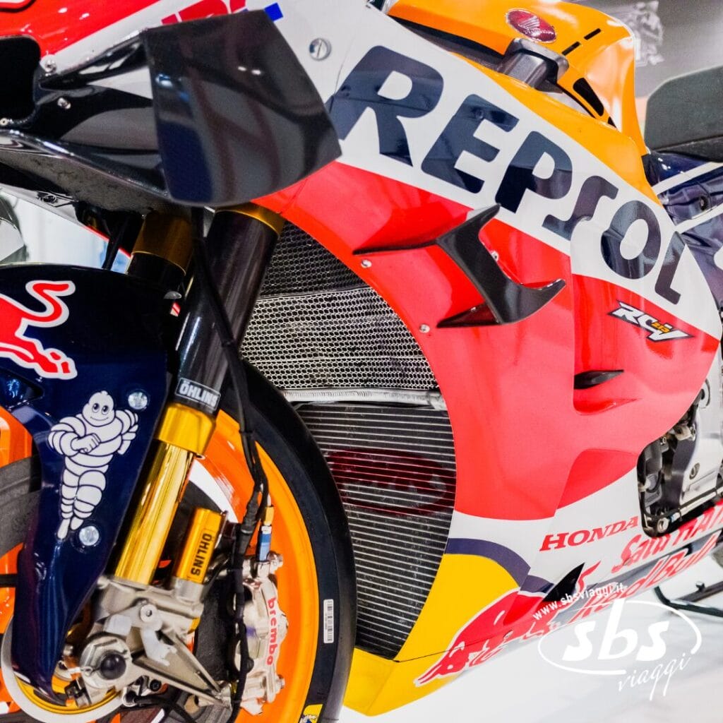 Primo piano della sezione anteriore di una moto da corsa Honda Repsol MotoGP, con in evidenza le ruote, le sospensioni e i loghi dettagliati degli sponsor.