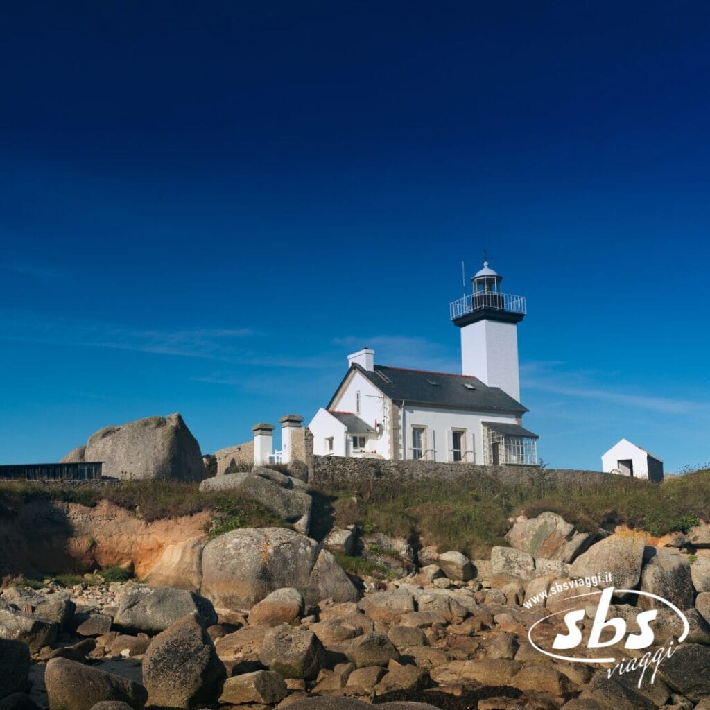 Un faro bianco con una casa annessa si erge su un paesaggio costiero roccioso sotto un cielo azzurro e limpido, offrendo una tappa pittoresca per qualsiasi avventura del Tour Scozia o delle Orcadi.