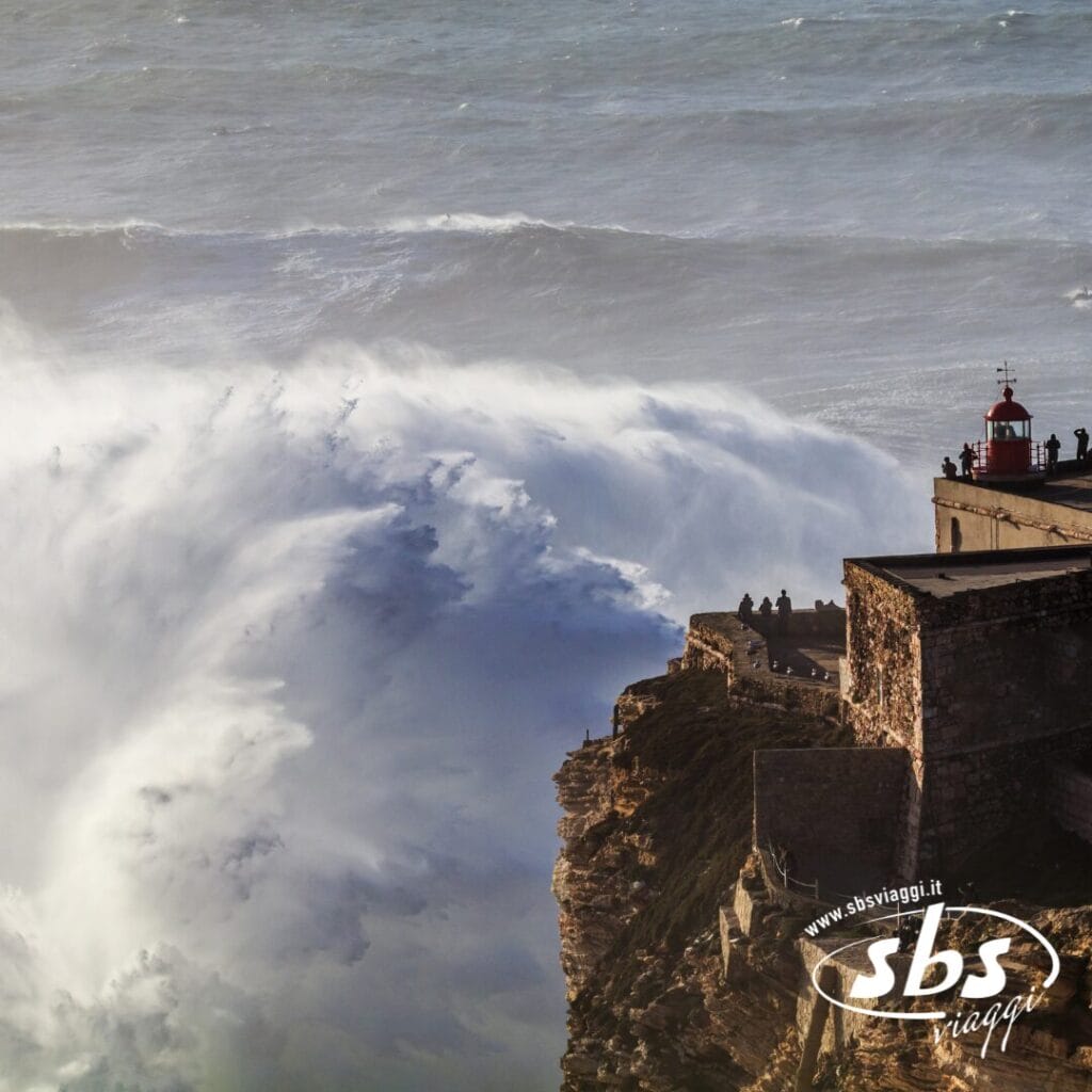 Enormi onde oceaniche si infrangono contro una scogliera rocciosa nei pressi di un faro, dove il Tour Portogallo Express porta i visitatori ad ammirare la scena dall'alto.