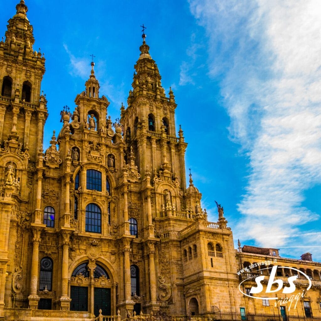 La facciata decorata di una cattedrale storica di Santiago si erge con le sue alte torri e le sue pietre lavorate nei minimi dettagli, contro un cielo azzurro con qualche nuvola: il momento clou di ogni tour in Portogallo.