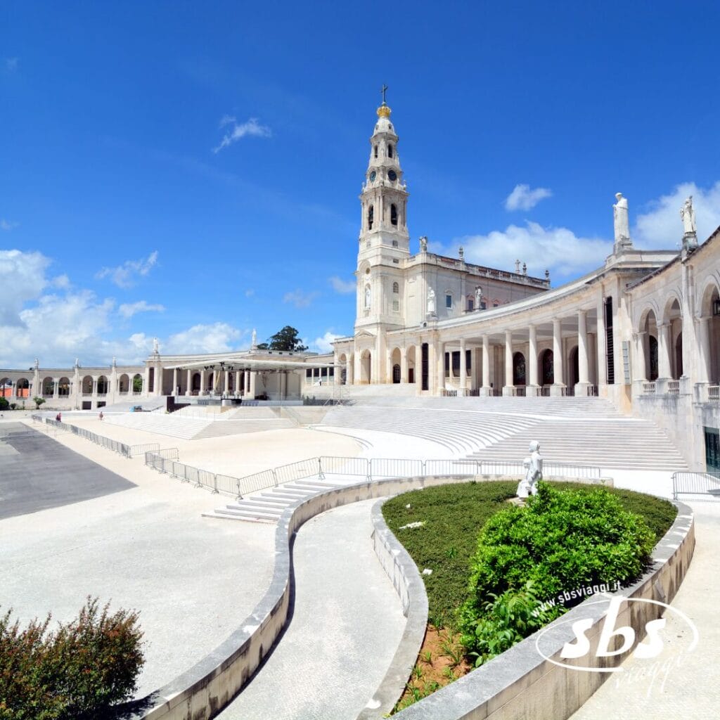 Un'ampia veduta del Santuario di Fátima in Portogallo, con la basilica centrale, i colonnati e una grande piazza aperta sotto un cielo azzurro brillante: una tappa iconica di un tour memorabile.