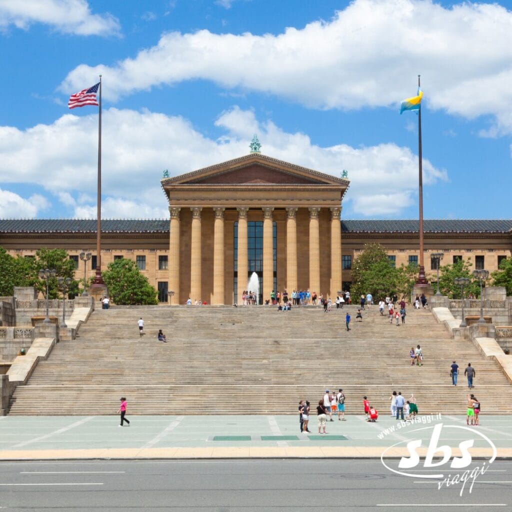 Il Philadelphia Museum of Art, tappa obbligata di ogni tour della costa orientale, è caratterizzato da ampi gradini in pietra, persone che camminano e bandiere americane e cittadine che sventolano contro il cielo blu.