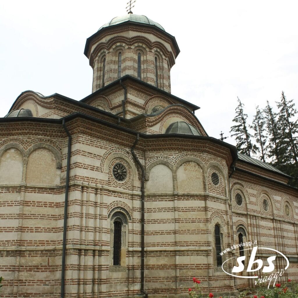 Una storica chiesa ortodossa orientale con muri in mattoni e pietra a strisce, finestre ad arco e un tetto a cupola, circondata da alberi: una tappa obbligata in qualsiasi tour della Bulgaria.