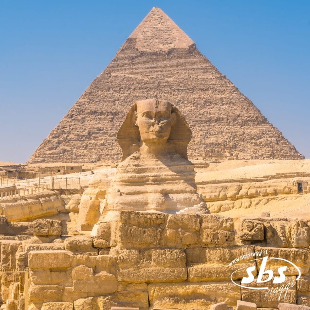 La Grande Sfinge si erge davanti alla Piramide di Chefren a Giza, in Egitto, immersa nella luce del sole: un'iconica meraviglia dell'Antico Egitto. Il logo di sbsviaggi appare nell'angolo, invitandovi a iniziare il vostro indimenticabile tour.