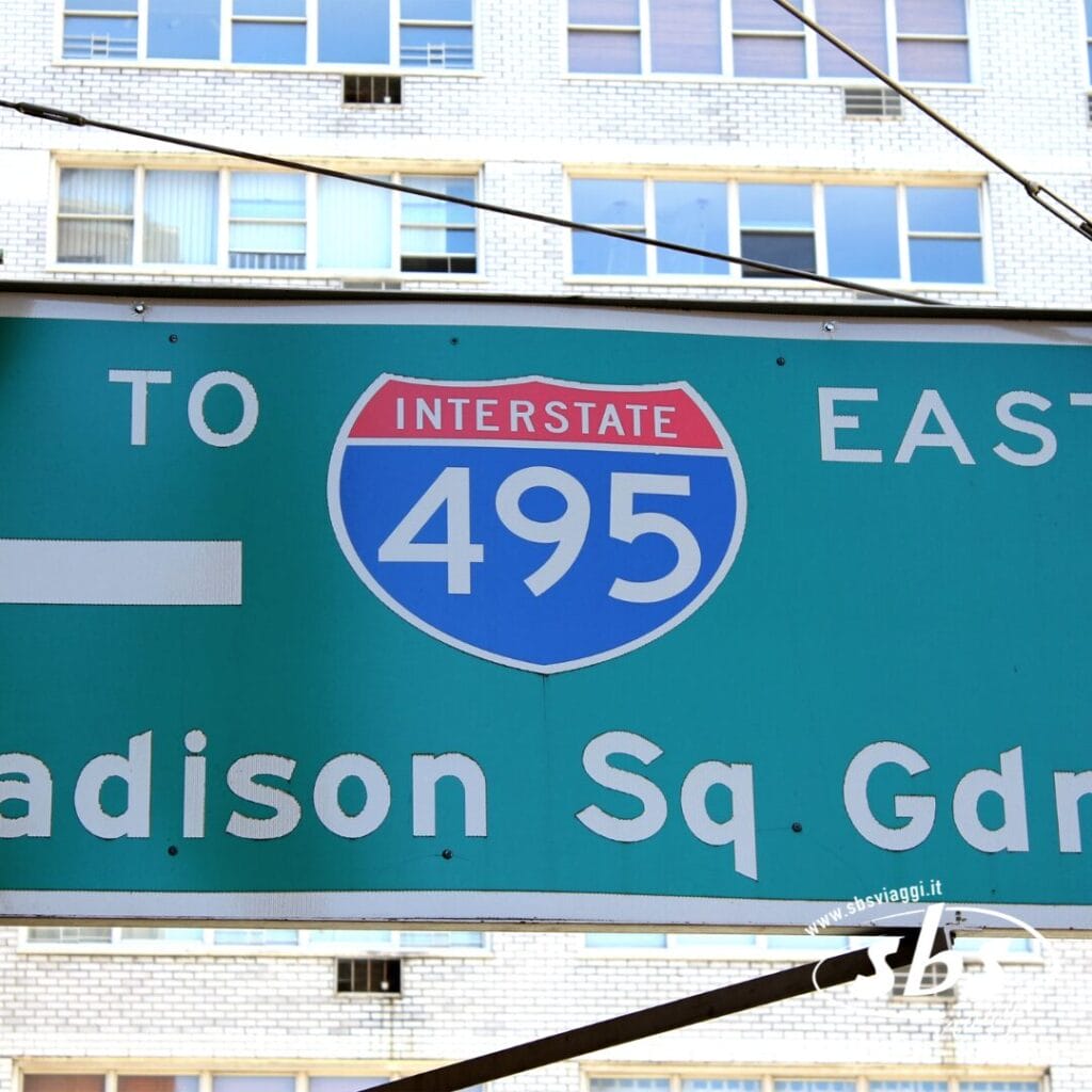 Cartello stradale verde per l'Interstate 495 East e il Madison Square Garden, teatro di momenti indimenticabili dell'NBA, con parte di un edificio visibile sullo sfondo.