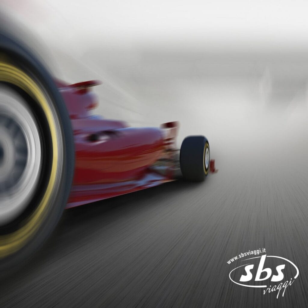 Primo piano di un'auto di Formula 1 rossa in pista, che cattura a pieno le emozioni in pista. Lo sfondo sfocato aggiunge un tocco di emozione, mentre il logo e il sito web di SBS viaggi compaiono nell'angolo in basso a destra. Momenti indimenticabili ti aspettano nel 2025!.