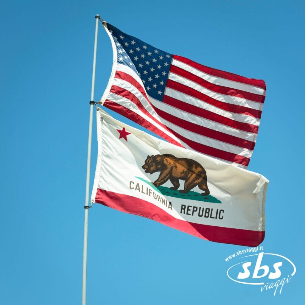 Due bandiere su pennoni contro un cielo azzurro: la bandiera degli Stati Uniti sopra la bandiera della Repubblica della California, a evocare l'orgoglio di Los Angeles, con il logo